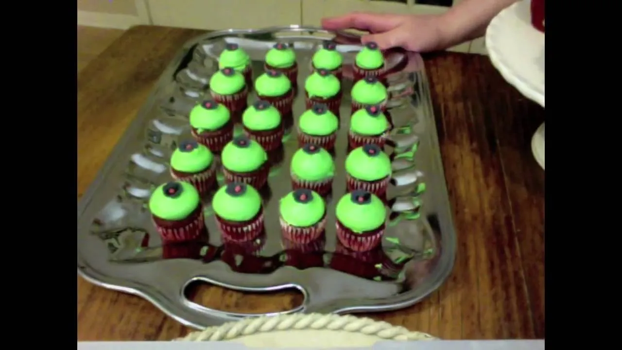 Tray of red cupcakes with green frosting and chocolate sprinkles.