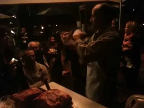 A chef presenting a dish to an engaged audience at a nighttime outdoor event.
