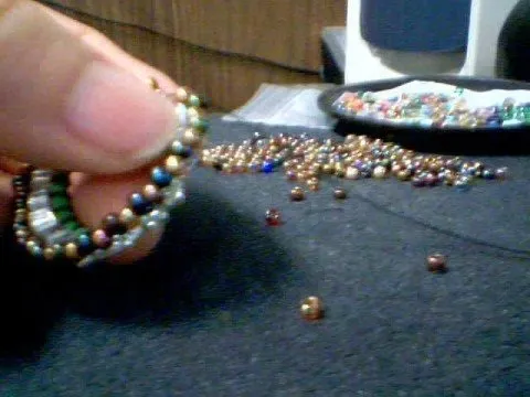 A hand holding a colorful beaded bracelet surrounded by scattered beads.