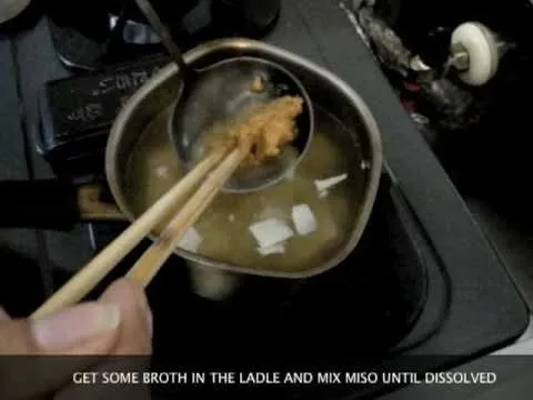 Mixing miso in broth using a ladle and chopsticks.
