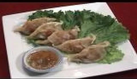 Steamed dumplings served with dipping sauce on a bed of lettuce.