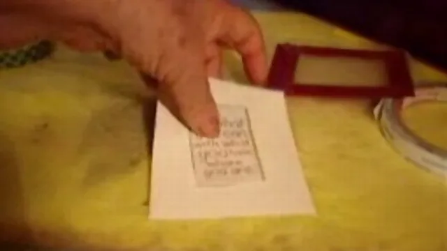 Hand holding a small card with printed text next to a red frame on a yellow surface.