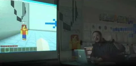 A person presenting a Minecraft game on a screen in a classroom setting.