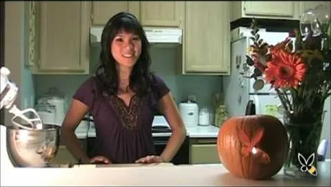 Woman standing in a kitchen with a carved pumpkin on the counter.