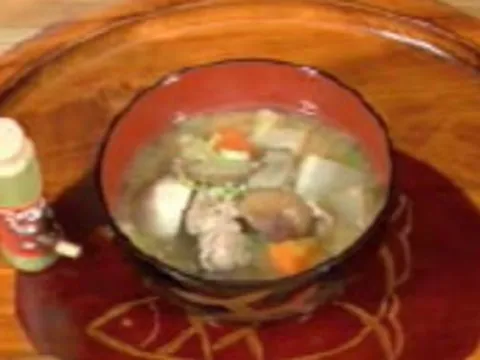 Bowl of soup with vegetables and meat on a wooden table.