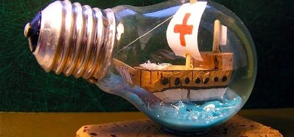 A miniature ship in a light bulb, floating on blue water.