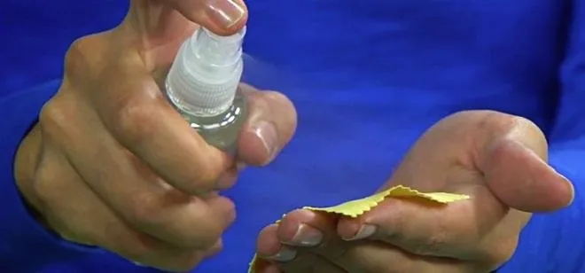 Person holding a spray bottle while applying a clear liquid to a yellow cloth.