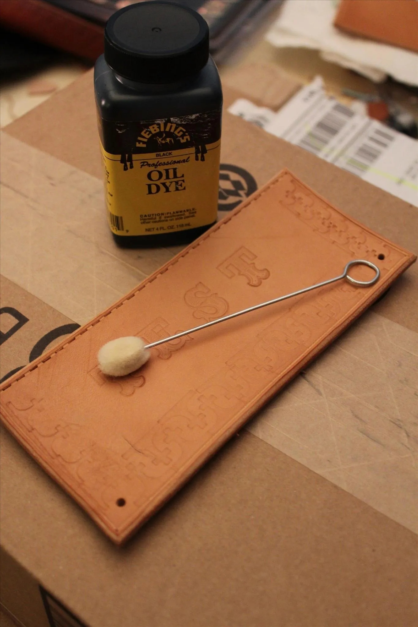 Crafting materials including a leather piece, a small spoon, and a bottle of dye.