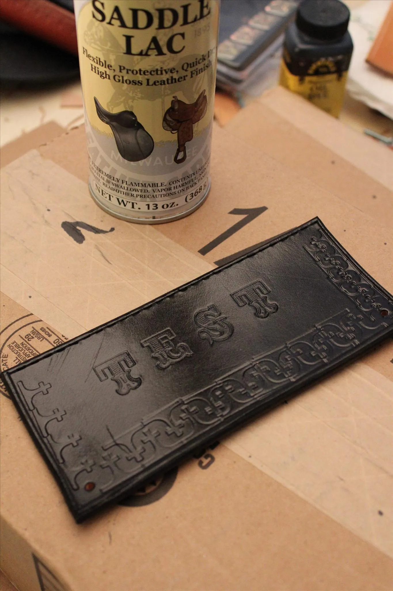 Leather piece with embossed design beside a can of saddle lac on a work surface.