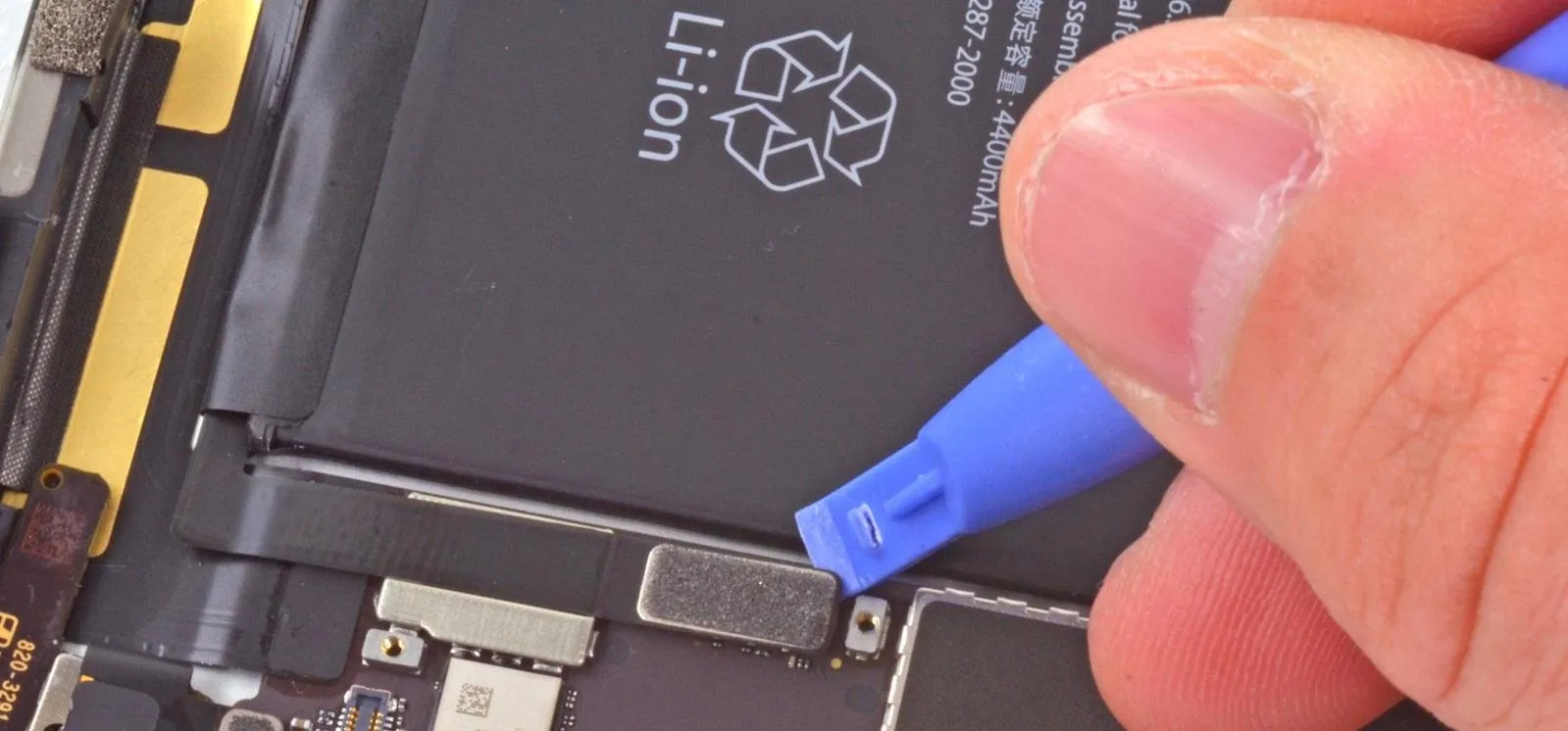 Hand using a plastic tool to disconnect a smartphone battery.