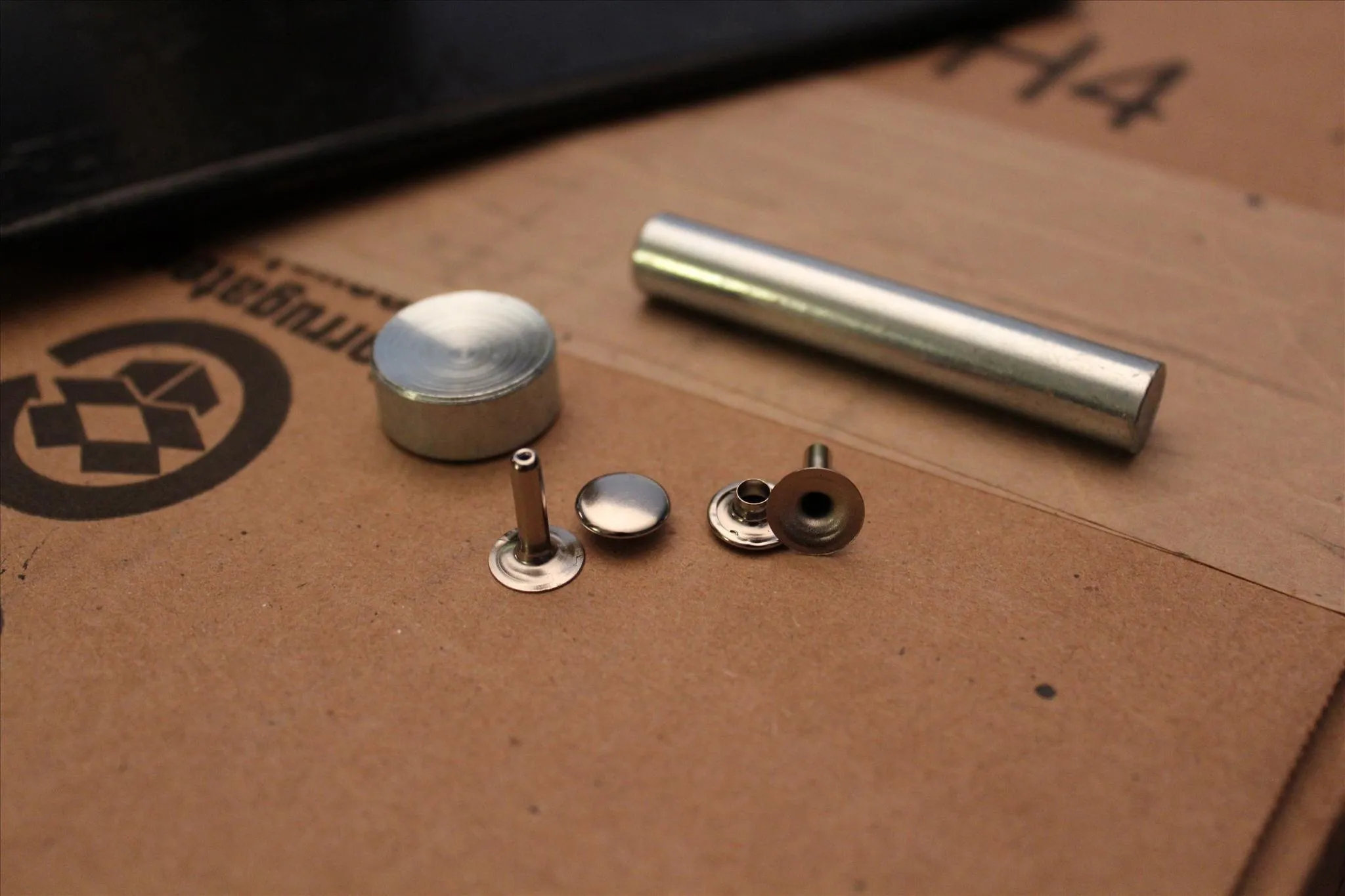 Metal components including screws, washers, and a cylinder on a brown surface.