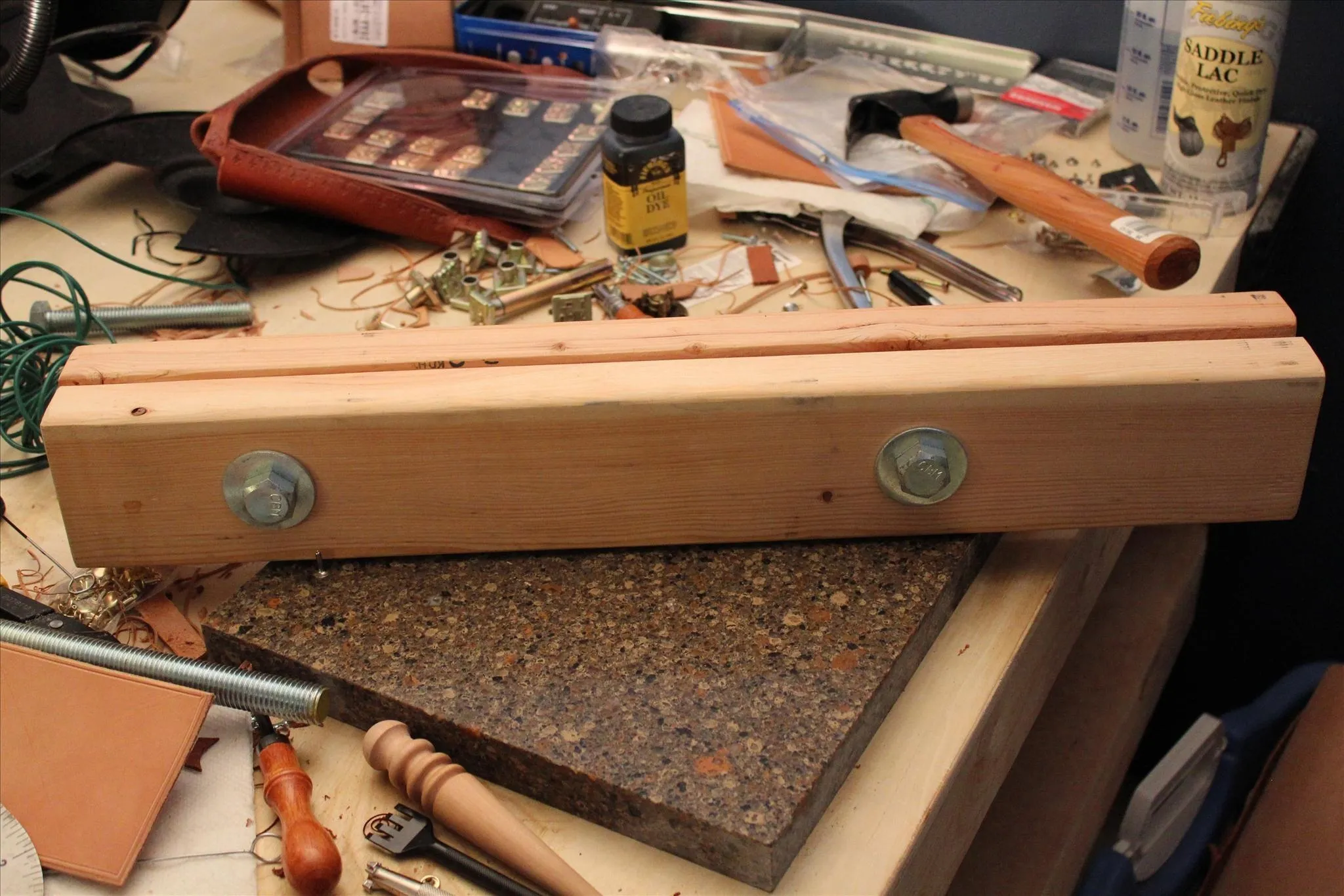 Wooden workpiece with metal fasteners on a cluttered workspace.