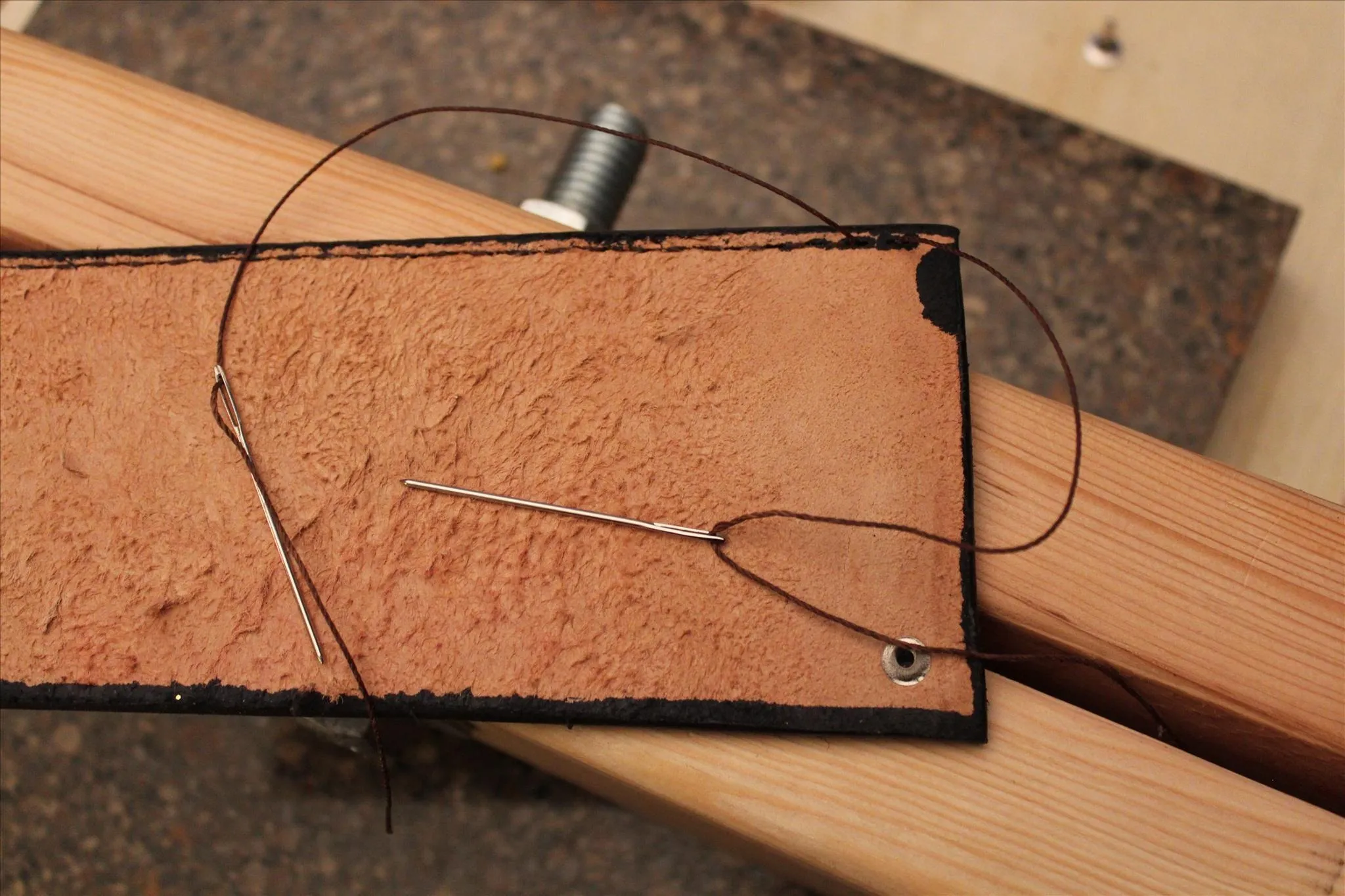 Leatherworking tools with a stitched leather piece on a wooden surface.