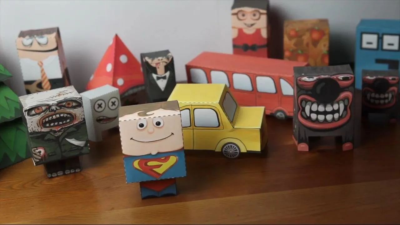 Paper toys and figures, including a superhero, car, and various characters displayed on a wooden surface.