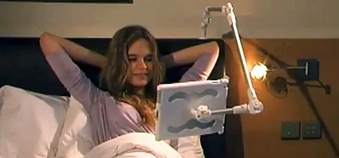 Woman relaxing in bed while using a tablet mounted on a stand.