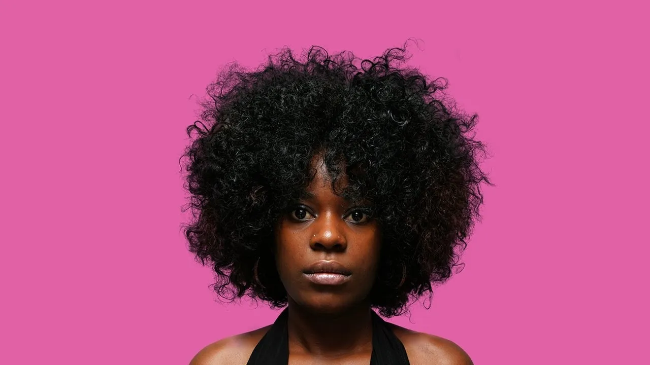 Woman with curly hair against a pink background.