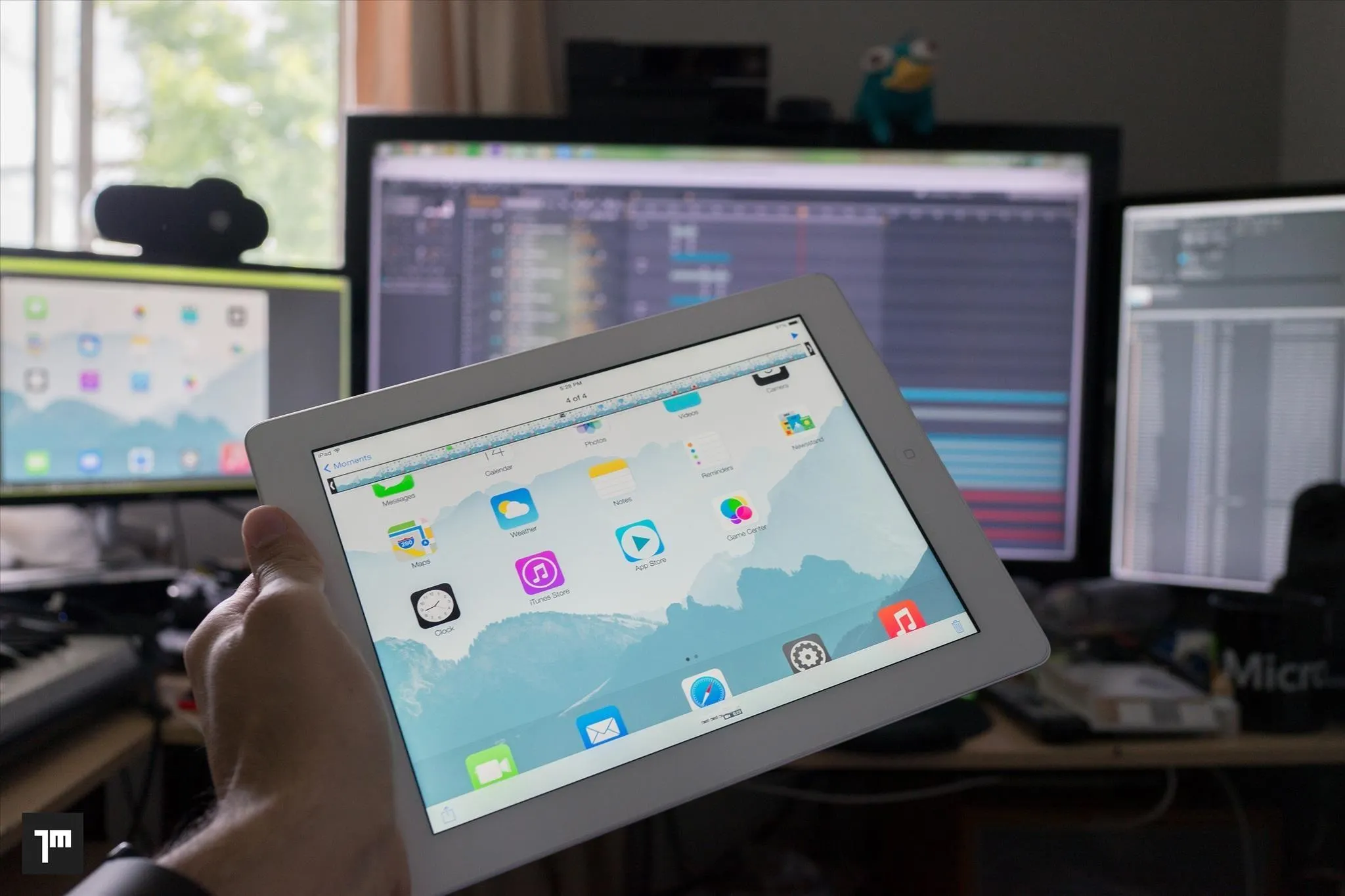 Person holding a tablet in a workspace with multiple computer screens.