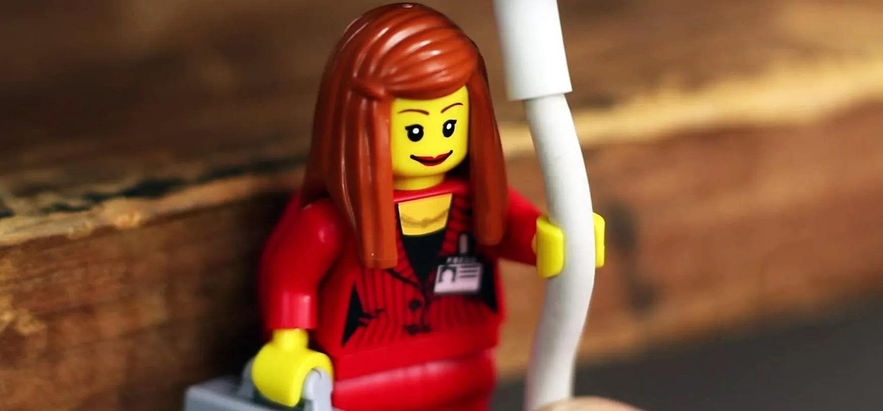 LEGO figure of a woman with long red hair, wearing a red outfit and holding a white pole.