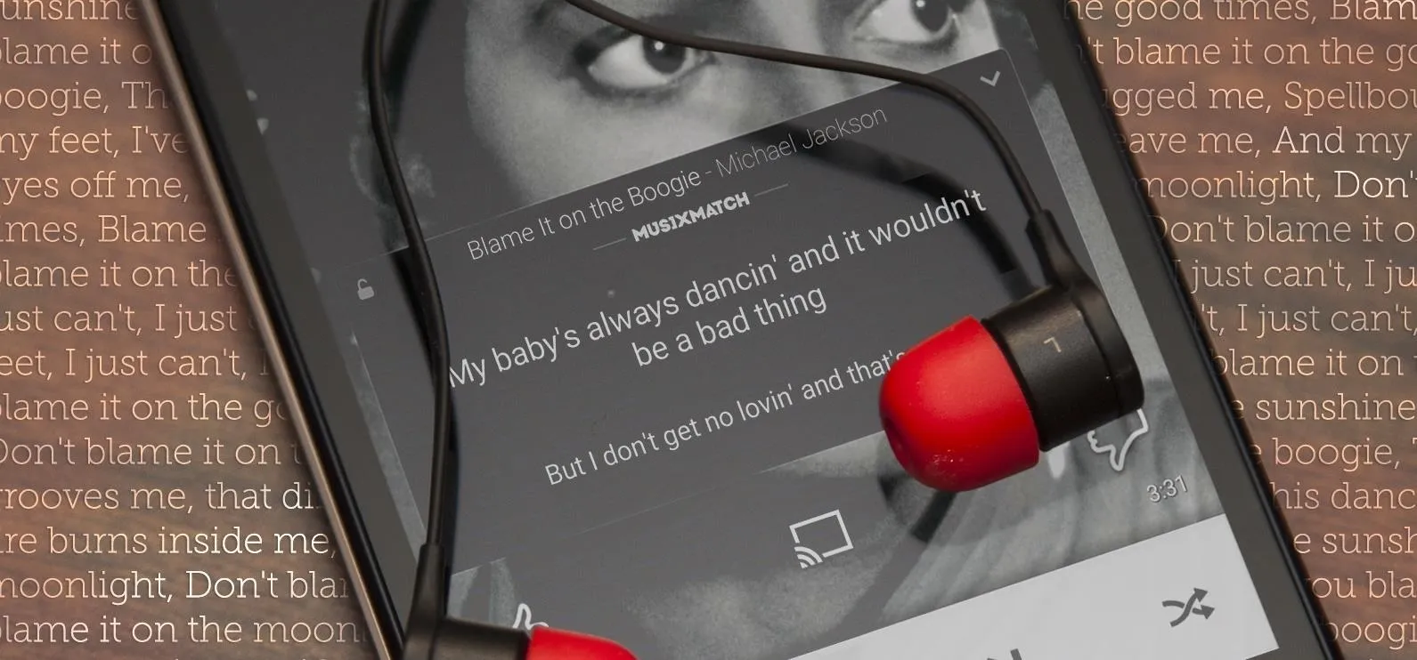 Close-up of a smartphone screen displaying lyrics with red earbuds resting on it.