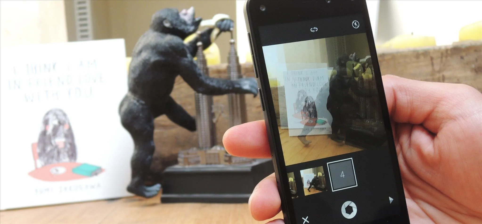 A hand holding a smartphone capturing an image of a gorilla statue with a drawing in the background.