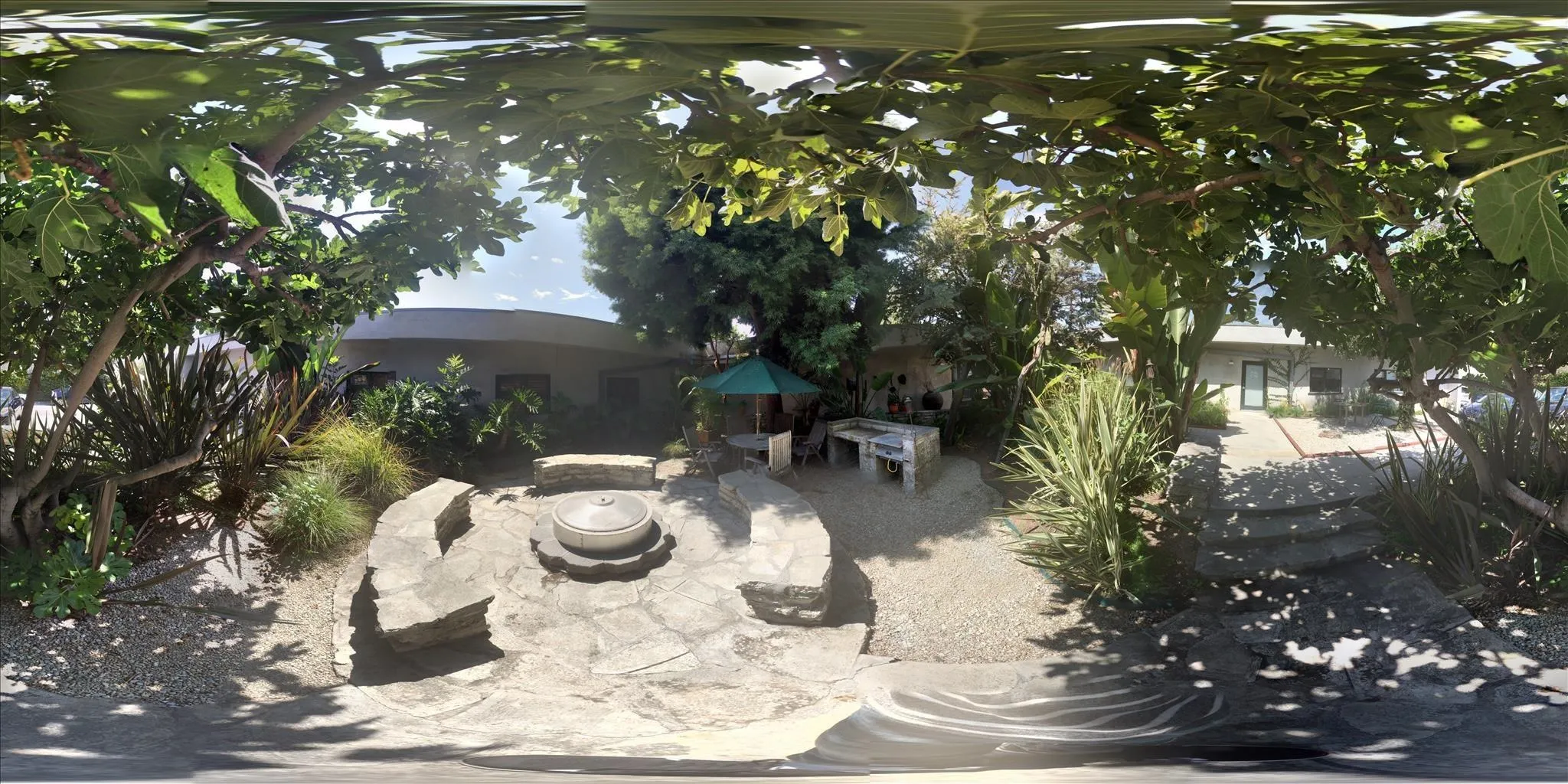 A serene outdoor garden space featuring a stone seating area, greenery, and an umbrella-covered table.