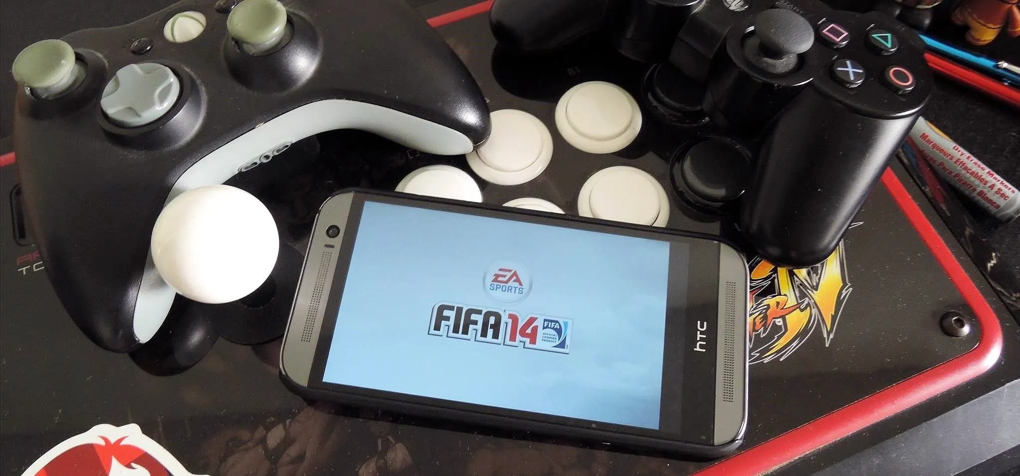 Mobile phone displaying FIFA 14 alongside gaming controllers and accessories.