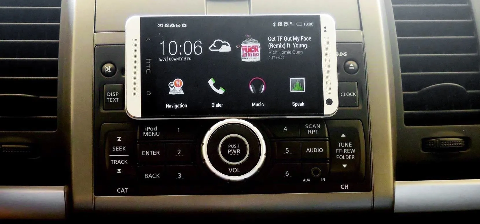 Smartphone mounted on a car dashboard display with control buttons.