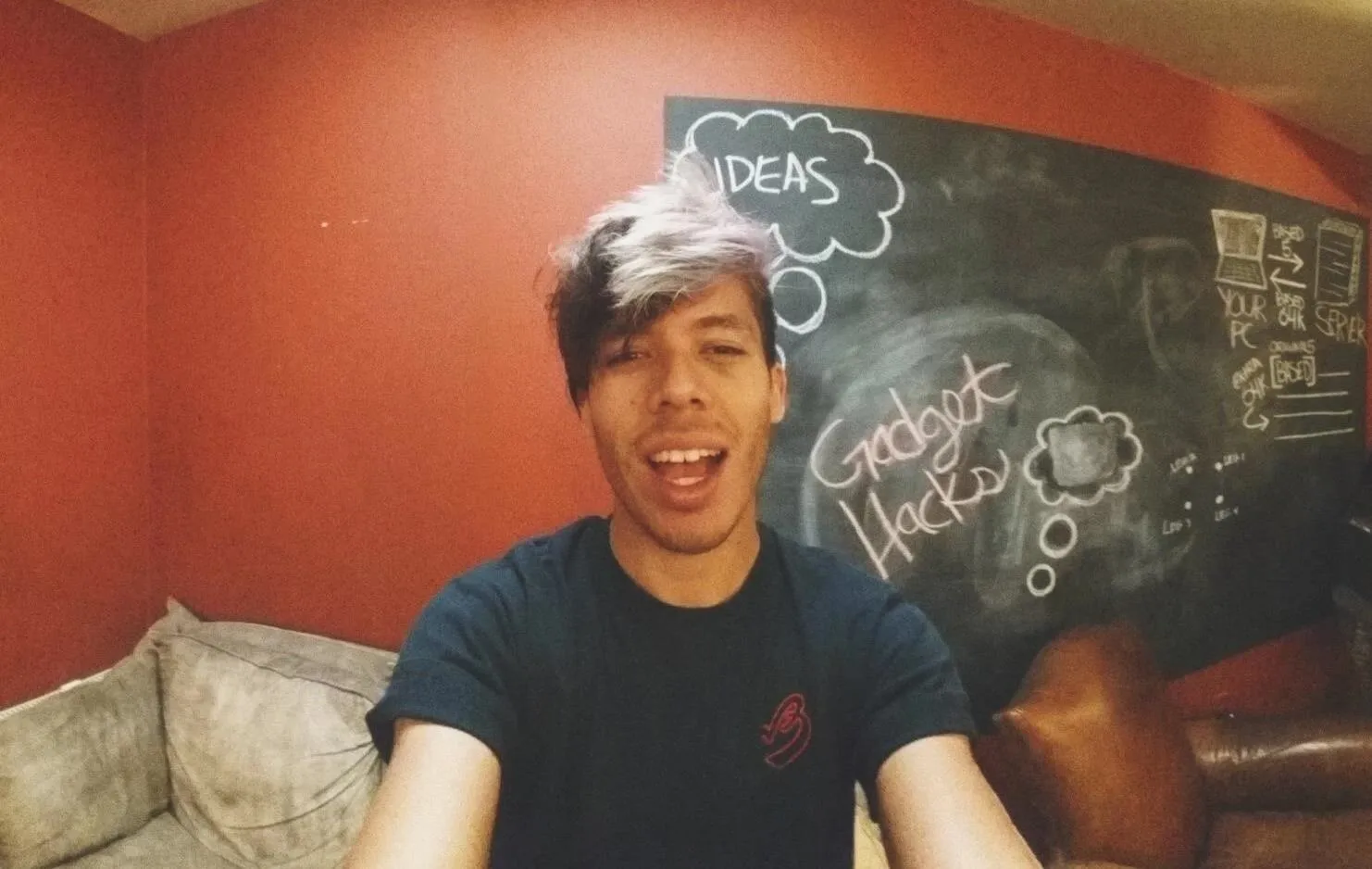 Young man smiling in front of a chalkboard with the word "Ideas" and a thought bubble drawn on it.
