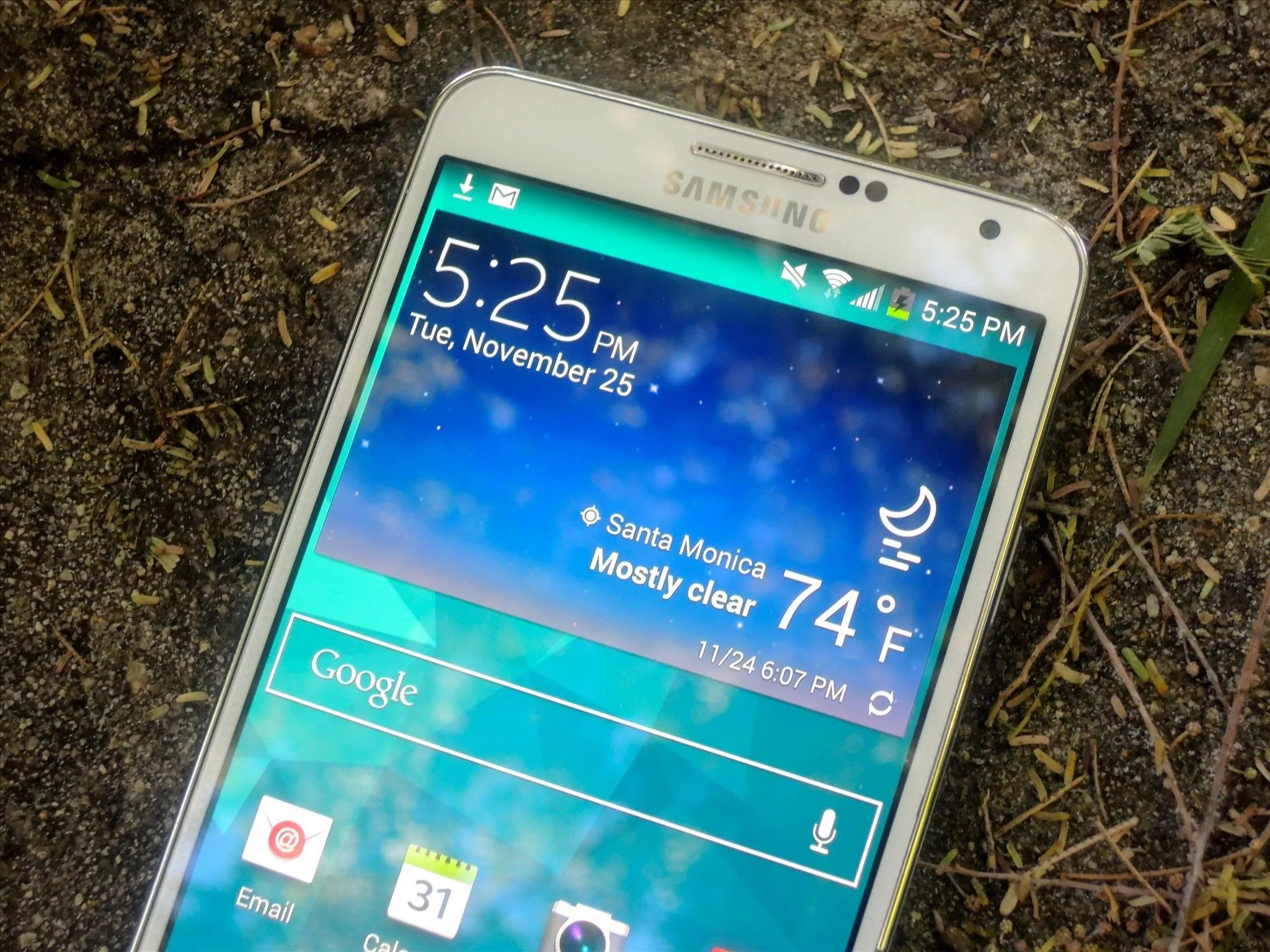 Smartphone displaying time, weather, and date on a natural background.