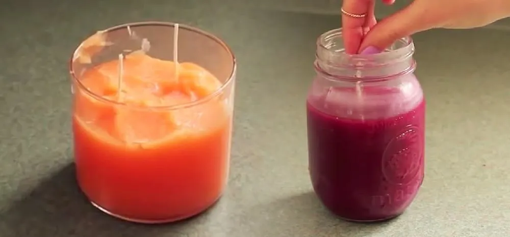 Homemade candles in orange and purple jars on a countertop.