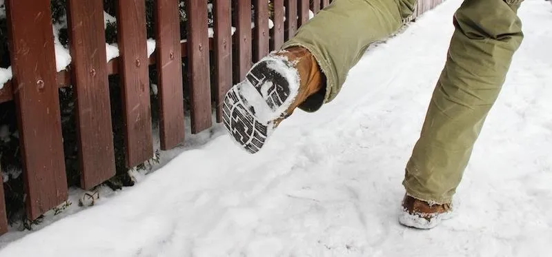 Person walking in the snow, showing footwear and a fence in the background.