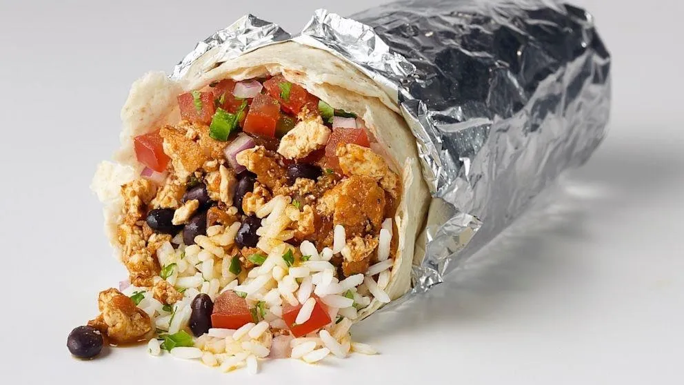 Burrito filled with rice, beans, tomatoes, and chicken, wrapped in foil.