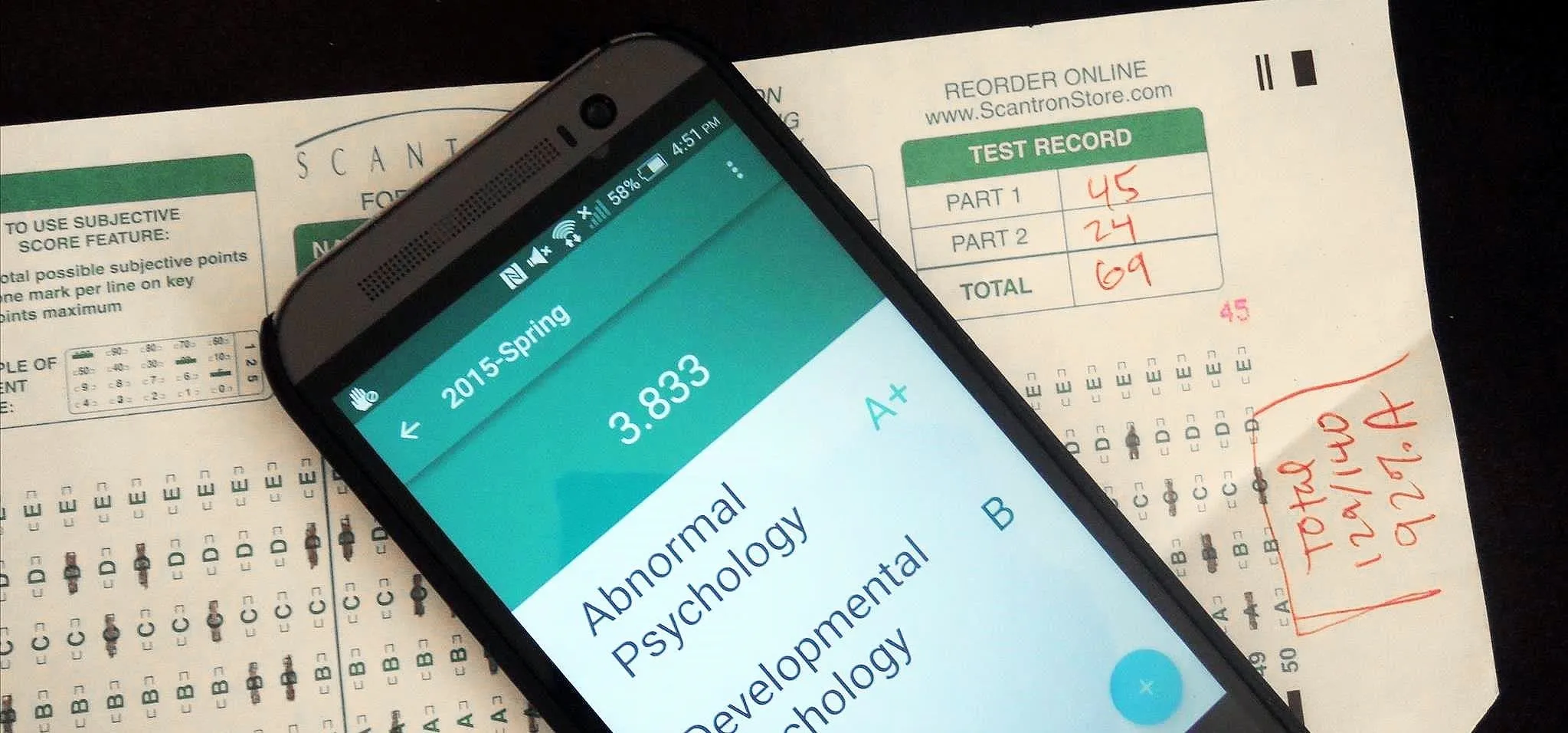 Smartphone displaying academic results on a paper with handwritten notes.