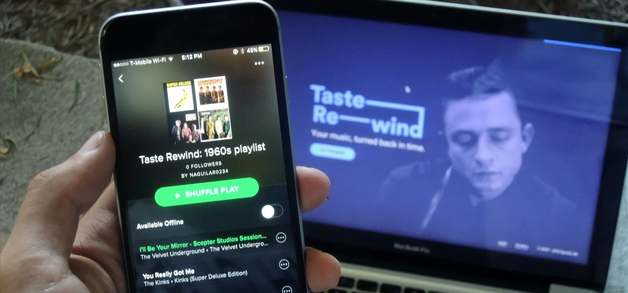 A person holding a smartphone showing a Spotify playlist, with a laptop displaying a music-themed website.