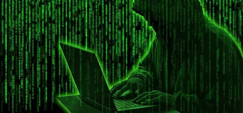 Silhouette of a person typing on a laptop with green code in the background.