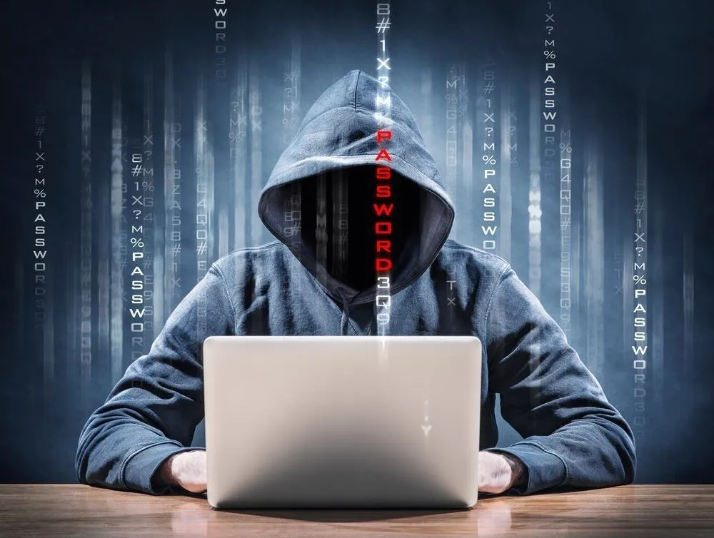 Person in a hooded sweatshirt using a laptop, with binary code in the background.