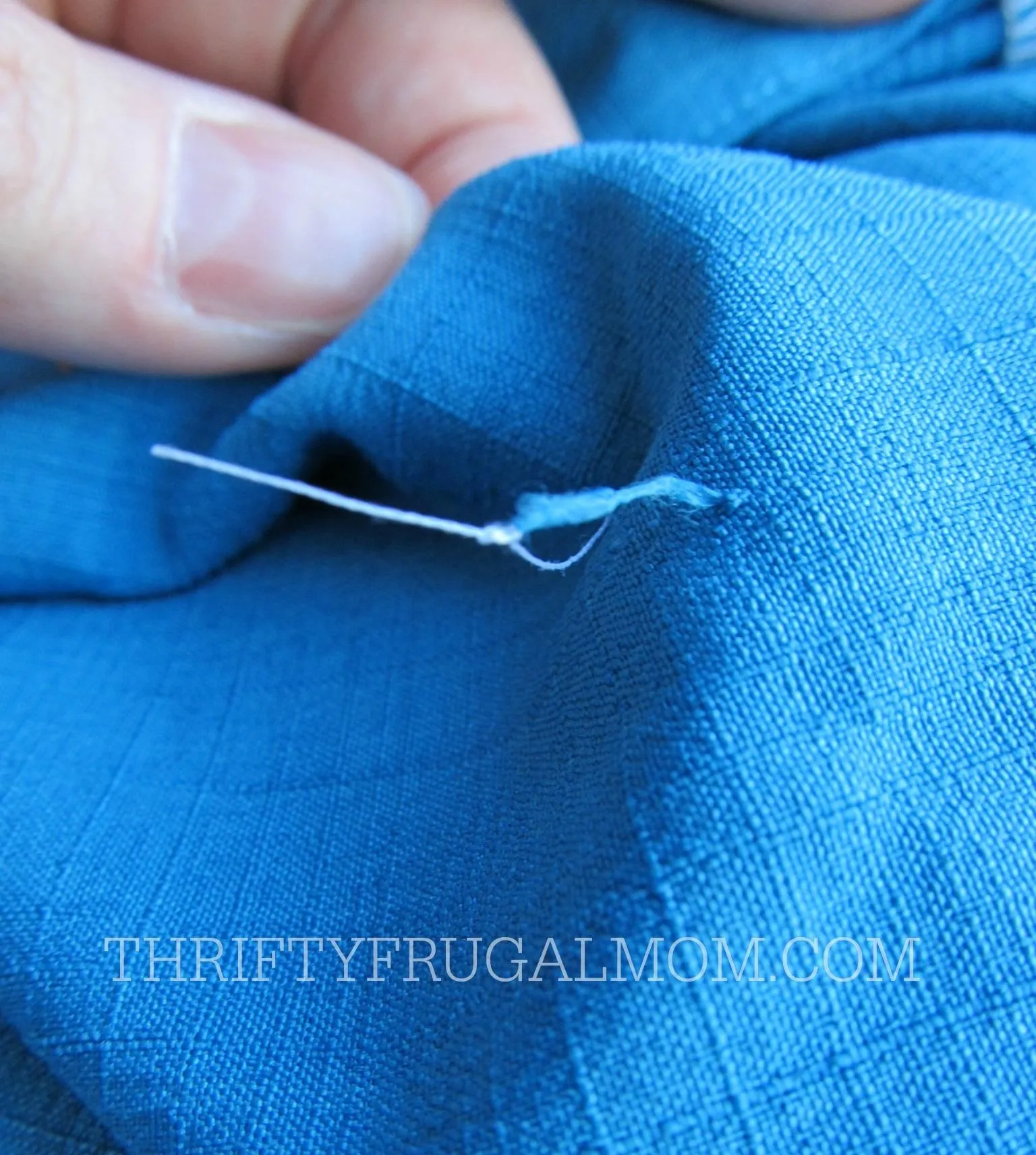 A close-up of a needle threaded through blue fabric.