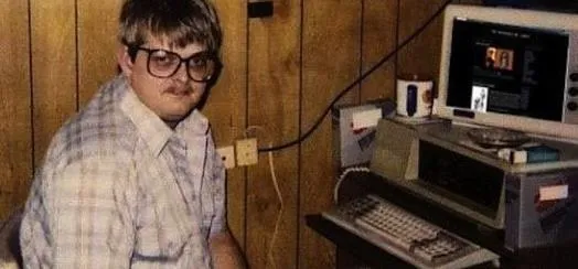 A person sitting at a vintage computer in a retro office setting.