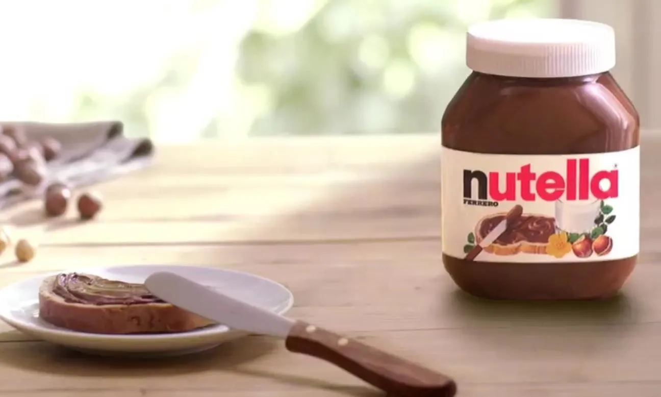 Nutella jar with a spread on a plate and a knife.