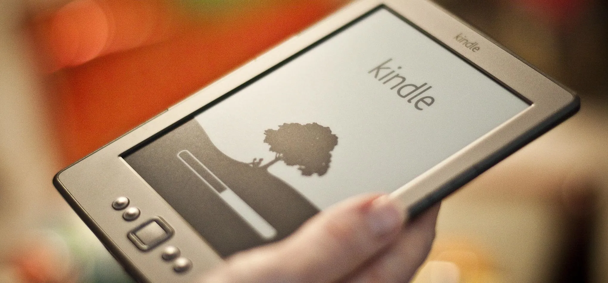 Hand holding a Kindle e-reader displaying a loading screen with a tree silhouette.