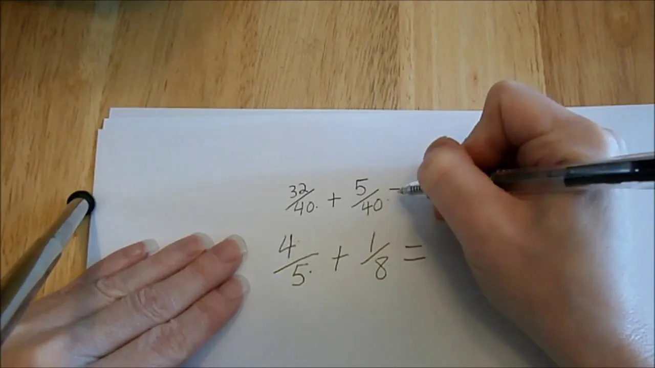 Hand writing a math problem involving fractions on a sheet of paper.