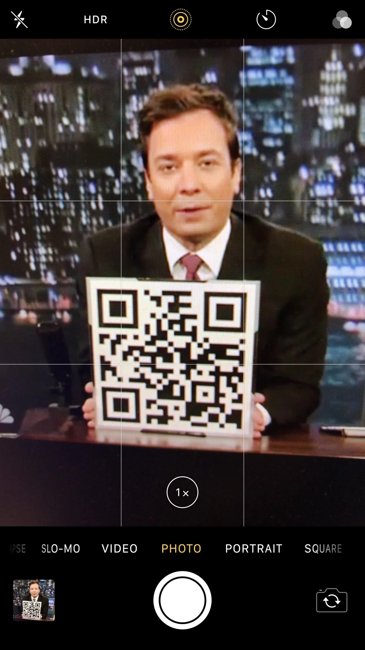 TV host holding a QR code in front of a city skyline background.