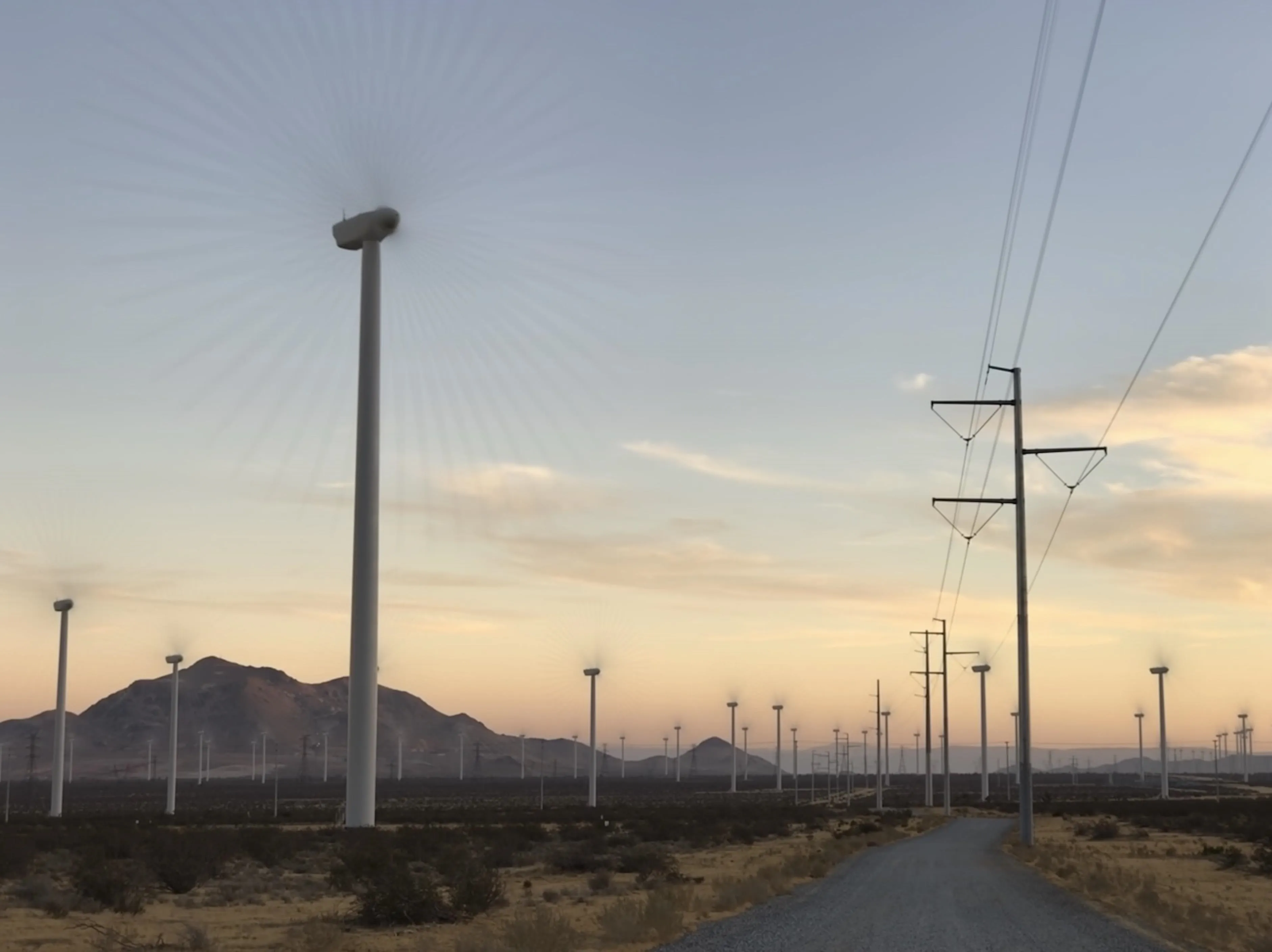 Wind turbines against a sunset landscape with power lines.