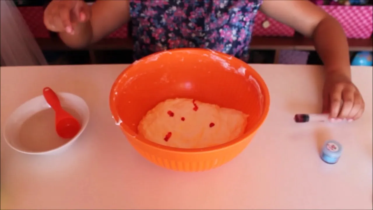A child mixing a colorful batter in an orange bowl on a table.