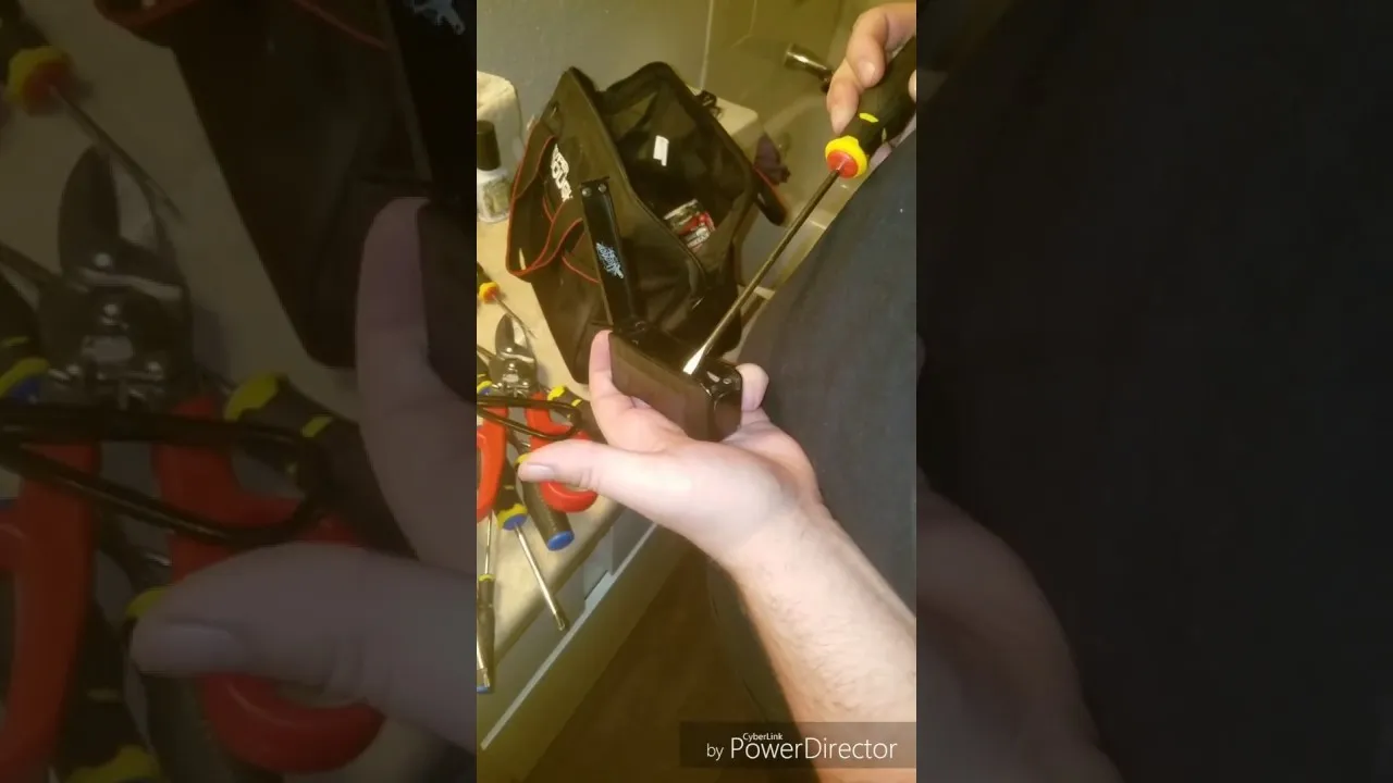 Hand holding a screwdriver with various tools in the background.