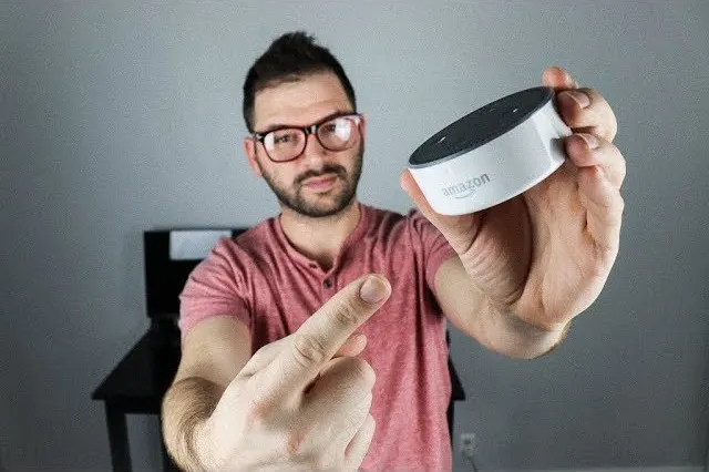 Man holding a smart speaker while pointing at it.