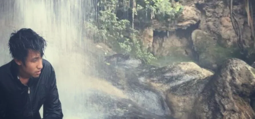 A person standing near a waterfall surrounded by rocks and greenery.