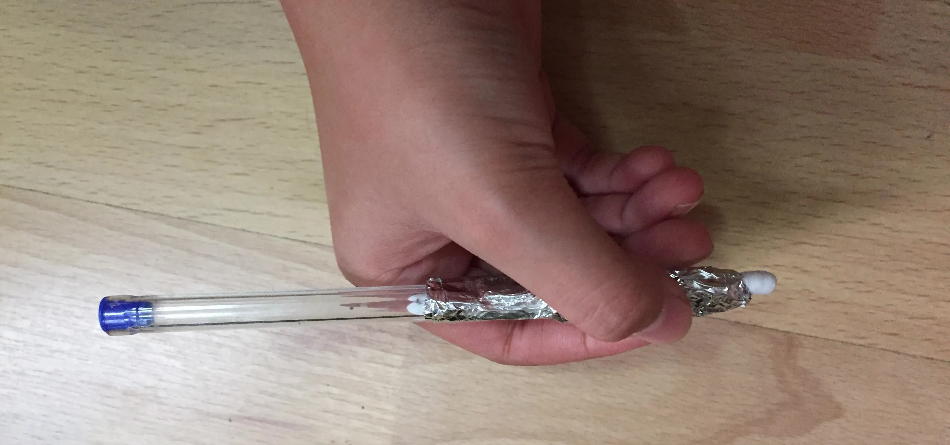 Hand holding a pen on a wooden surface.