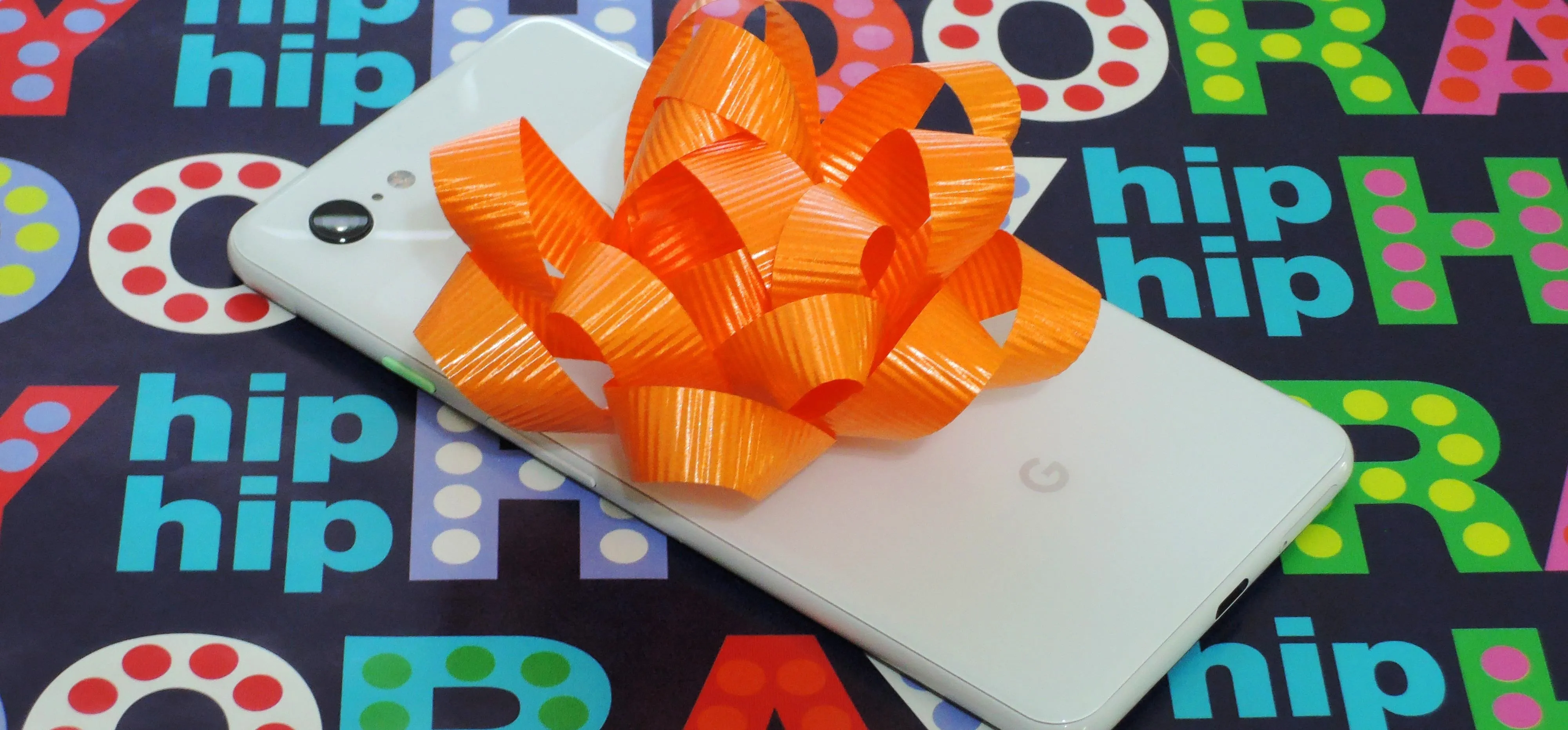 Smartphone with an orange bow on a colorful celebration background.