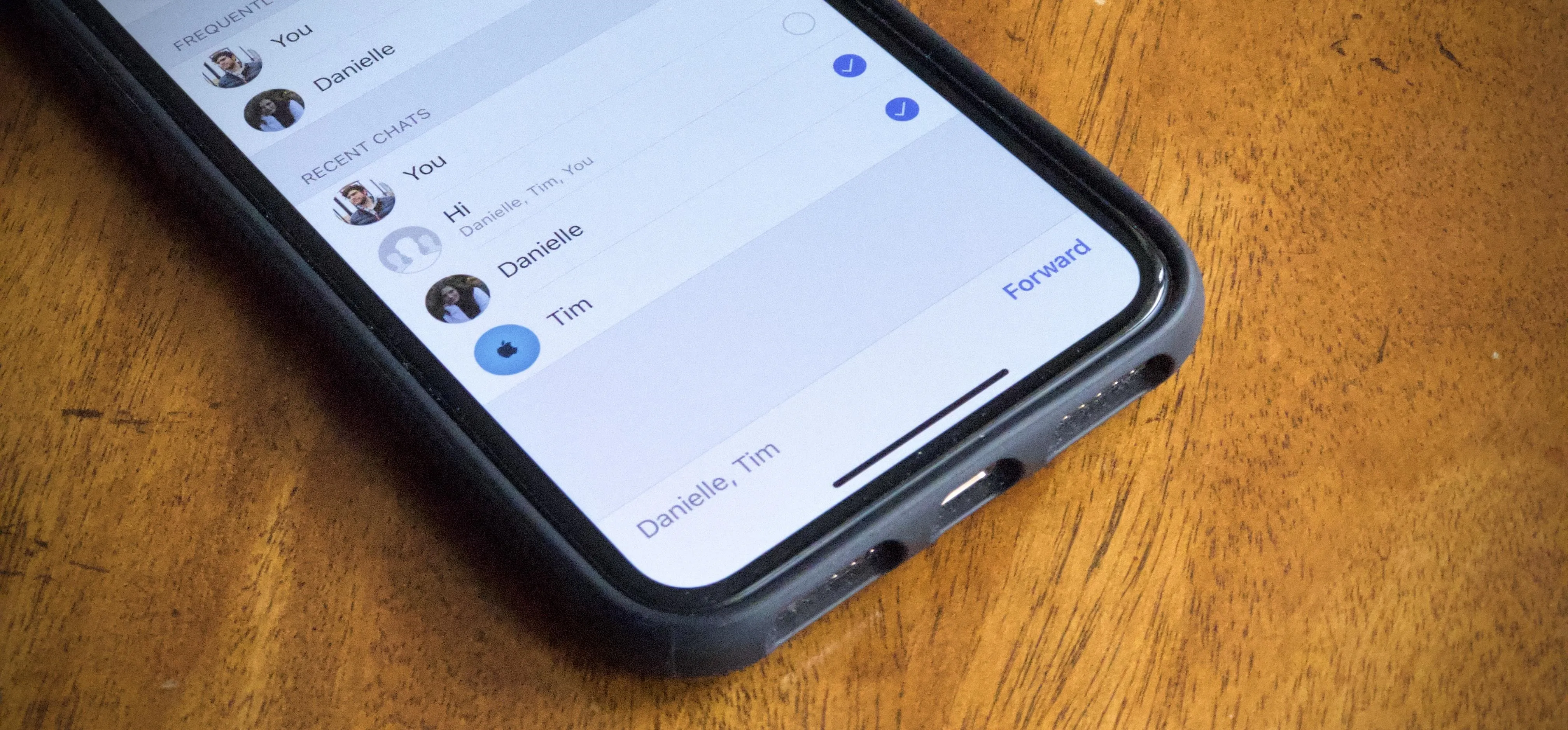 Close-up of a smartphone displaying a contact list on a wooden surface.